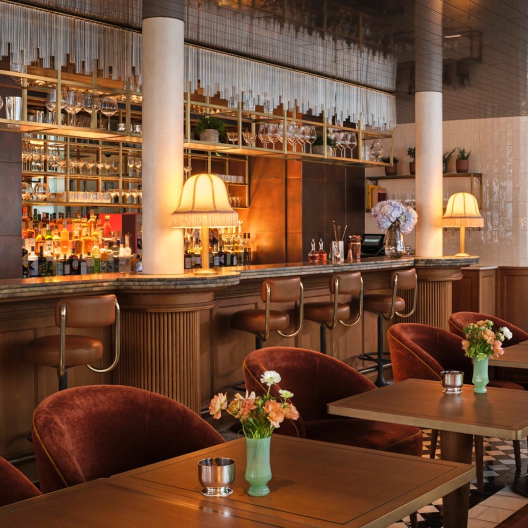 A Vienna bar with a well-stocked shelf of liquor bottles, bar stools, and tables with flowers.